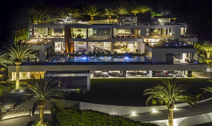 A mansion property with four levels and a pool, lit up at night
