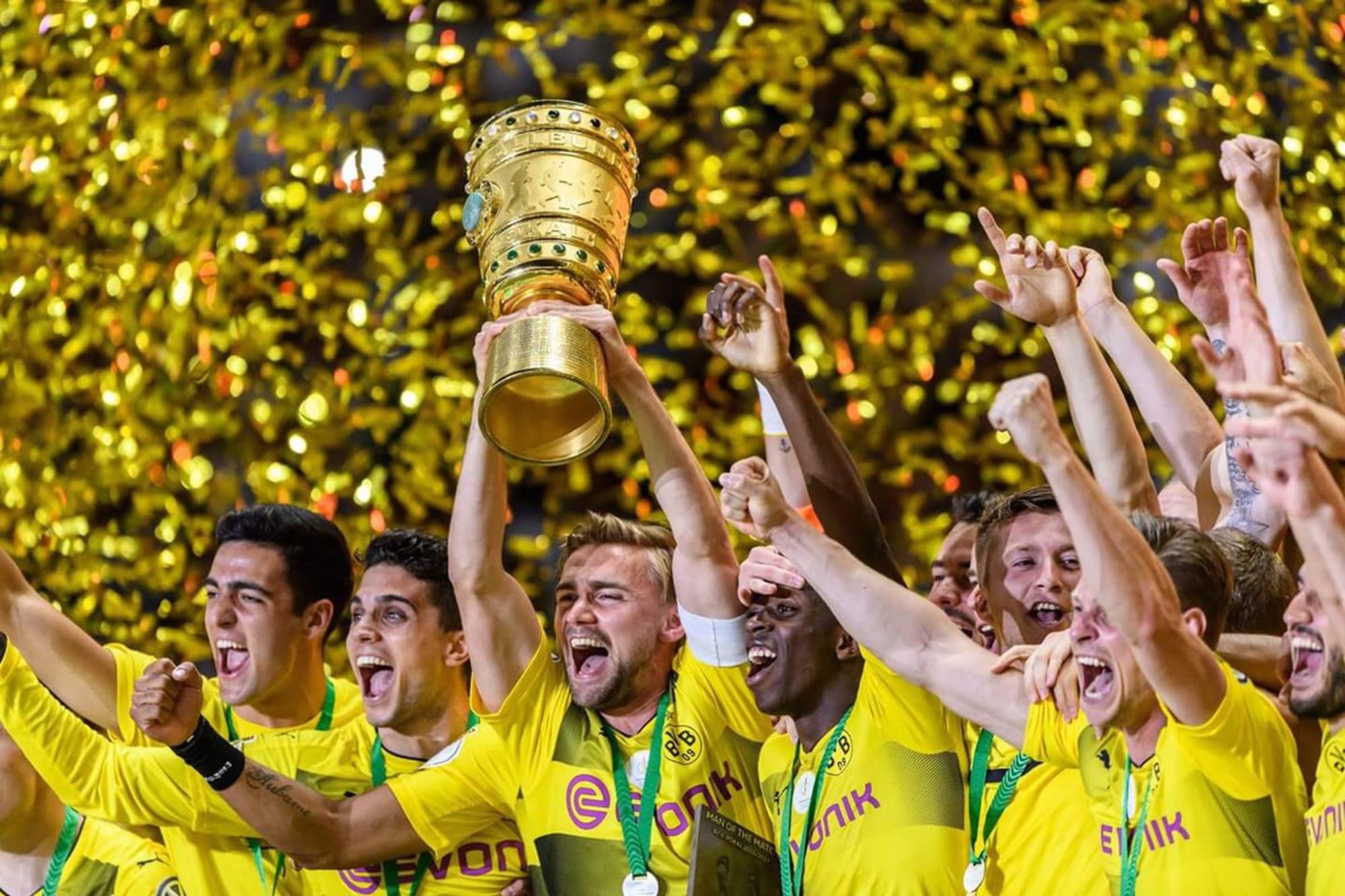  The image shows the football players of Borussia Dortmund celebrating their victory with the DFB-Pokal trophy in front of their cheering fans at Wembley Stadium.