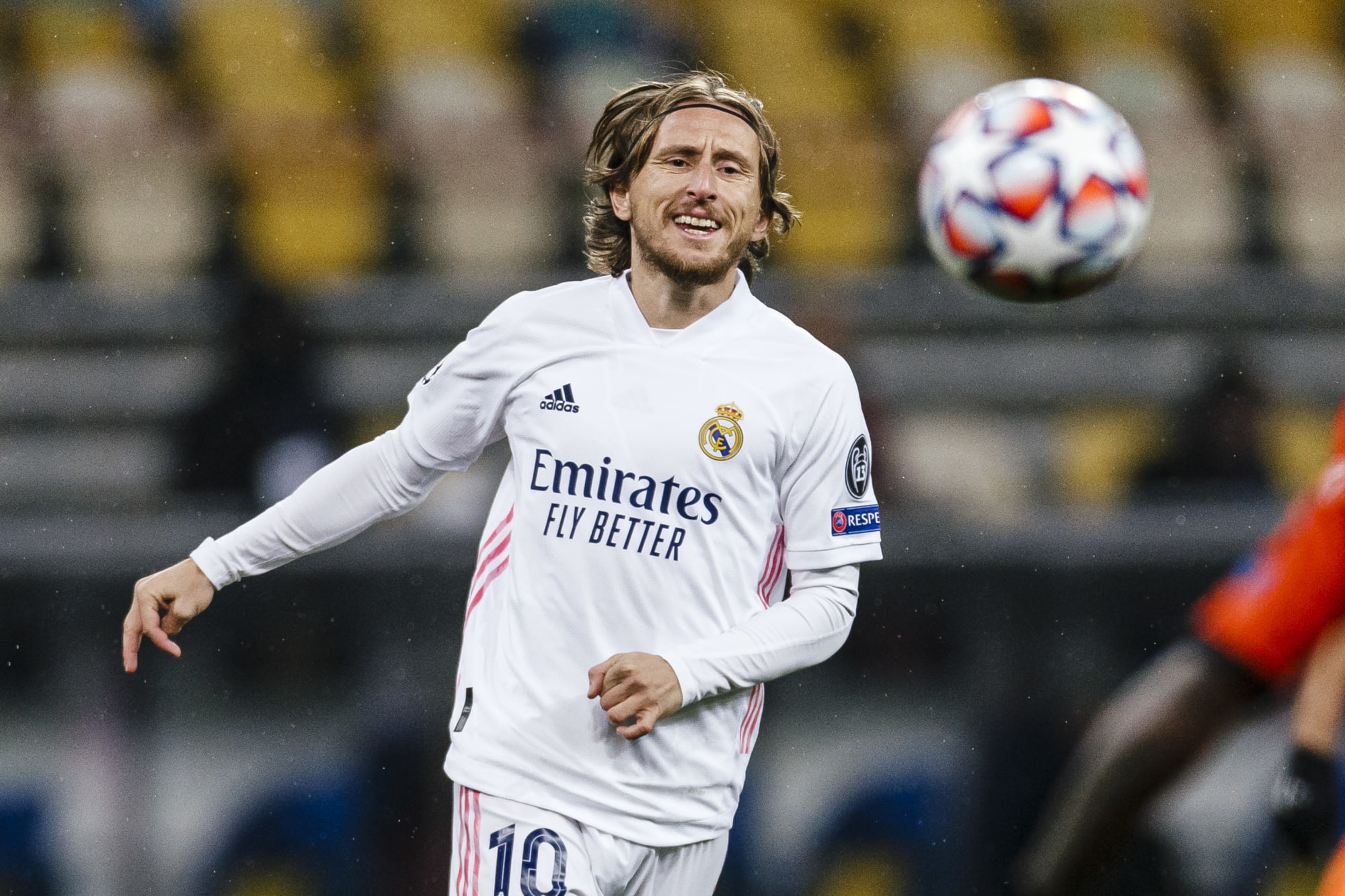  Luka Modric, a Croatian midfielder, is playing for Real Madrid in a white jersey with the number 10. He has long hair and is looking up at the ball.