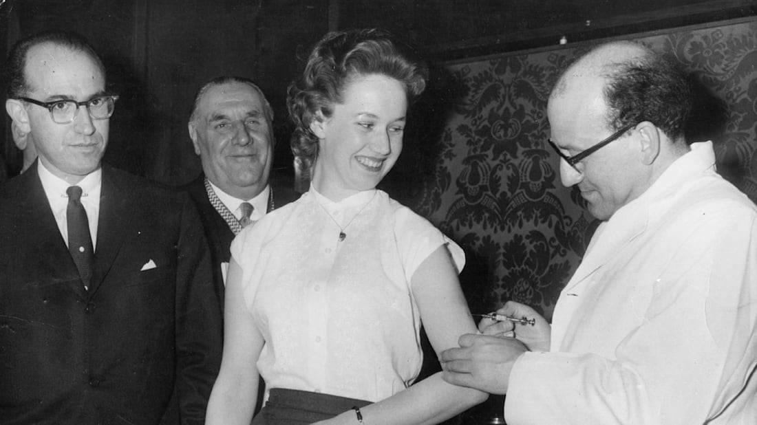 American doctor and epidemiologist Jonas Salk, who developed the first vaccine against poliomyelitis, looks on as a colleague gives the injection to a woman.