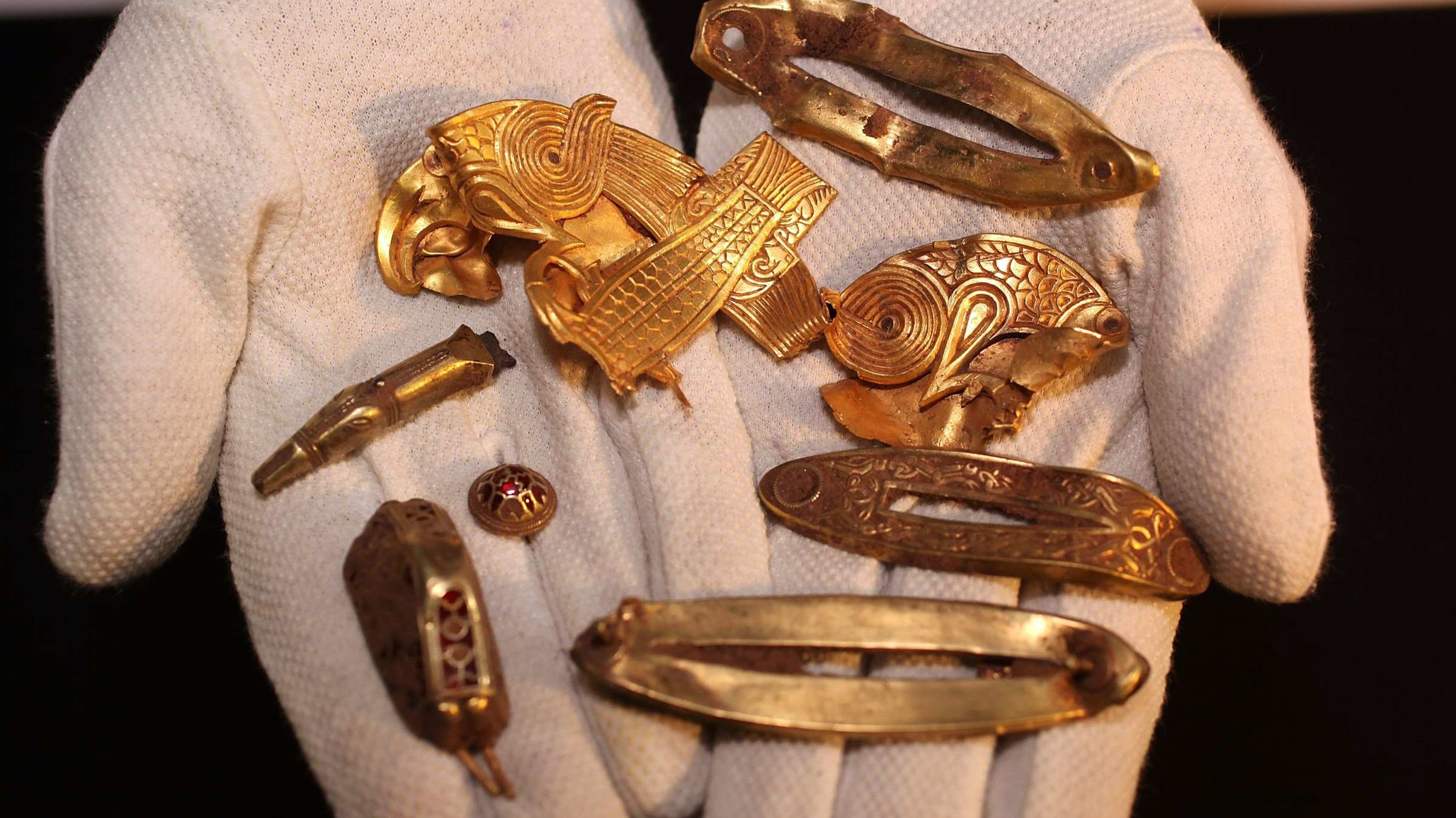  A photo of a gloved hand holding several gold and silver artifacts discovered by Polish archaeologist Romuald Ościak.