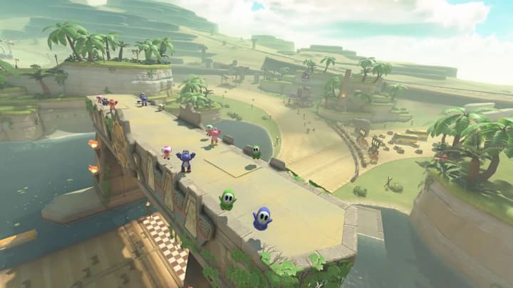 A track running through a deser with trees and grass starting to grow in Mario Kart World with Shy Guys and Yoshis watching.