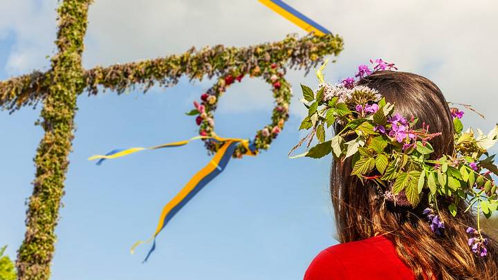 Woman with flower crown staring at Swedish cross at Midsommar festival