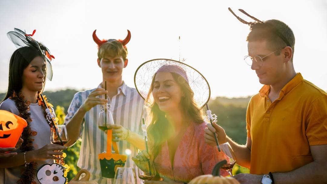 Friends in Halloween costumes celebrate together outdoors with drinks and decorations at a festive vineyard gathering. Friends in Halloween costumes celebrate together outdoors with drinks and decorations at a festive vineyard gathering.