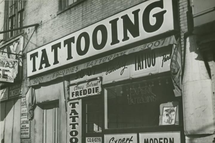 IRVING HERZBERG, TATTOO SHOP OF “CONEY ISLAND FREDDIE” JUST PRIOR TO NEW YORK CITY’S BAN ON TATTOOING, 1961, DIGITAL PRINT, BROOKLYN PUBLIC LIBRARY