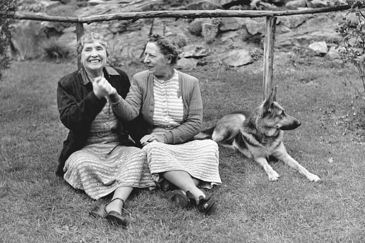 helen keller and polly thomson sitting in the grass with a german shepherd