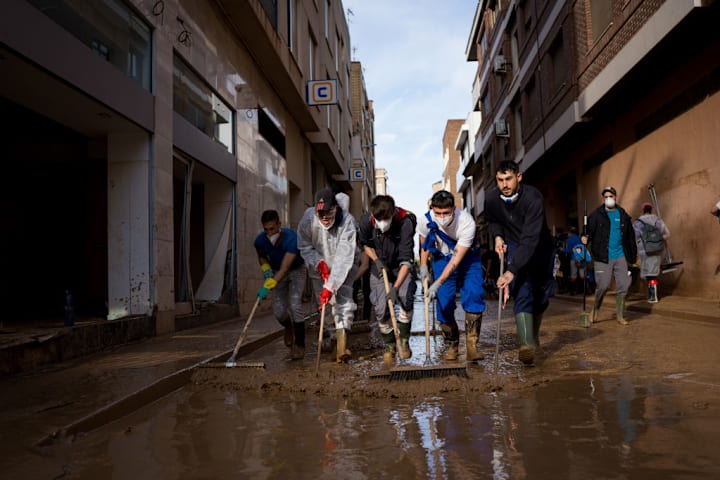 Volunteers are seen manually cleaning the street from the...