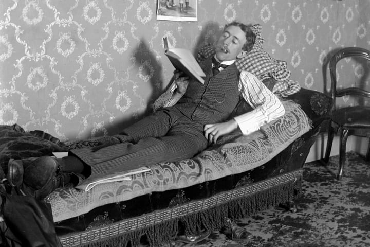 A lounging man reads a book, ca. 1900