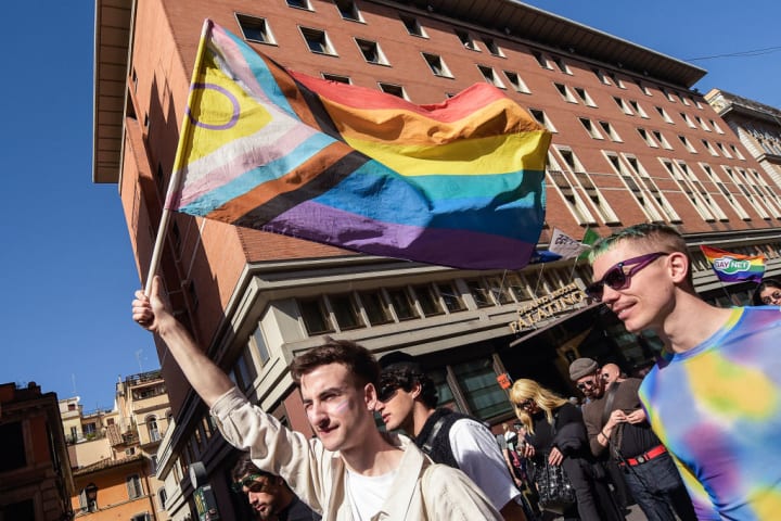 A person holds up an intersex-inclusive progress Pride flag.