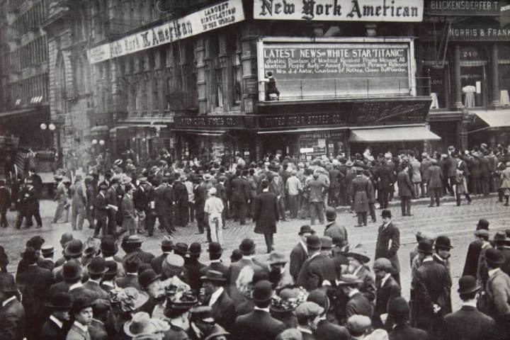 People gather at a newspaper billboard to read about the Titanic sinking