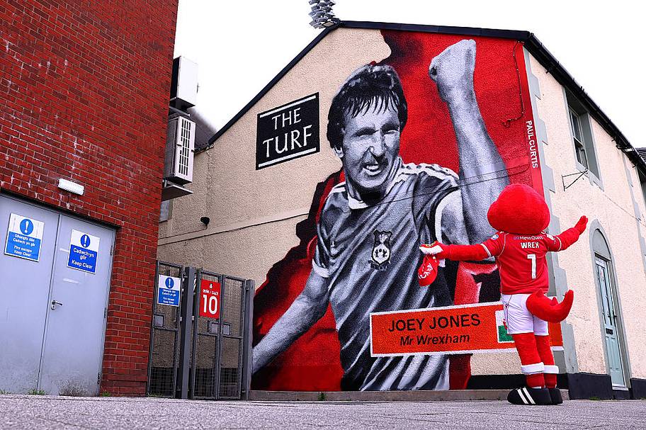 Wrex, Mascot of Wrexham, poses in front of a mural dedicated to Joey Jones Mr Wrexham outside The Turf 