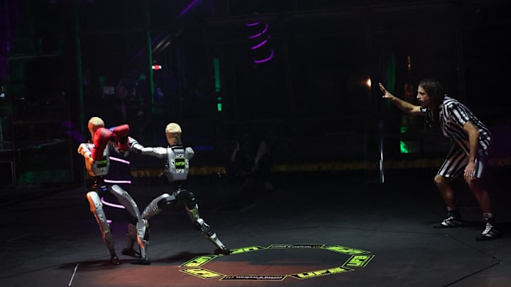 Un árbitro señala un punto mientras robots con guantes de boxeo intercambian golpes durante la Ultimate Fighting Bots.