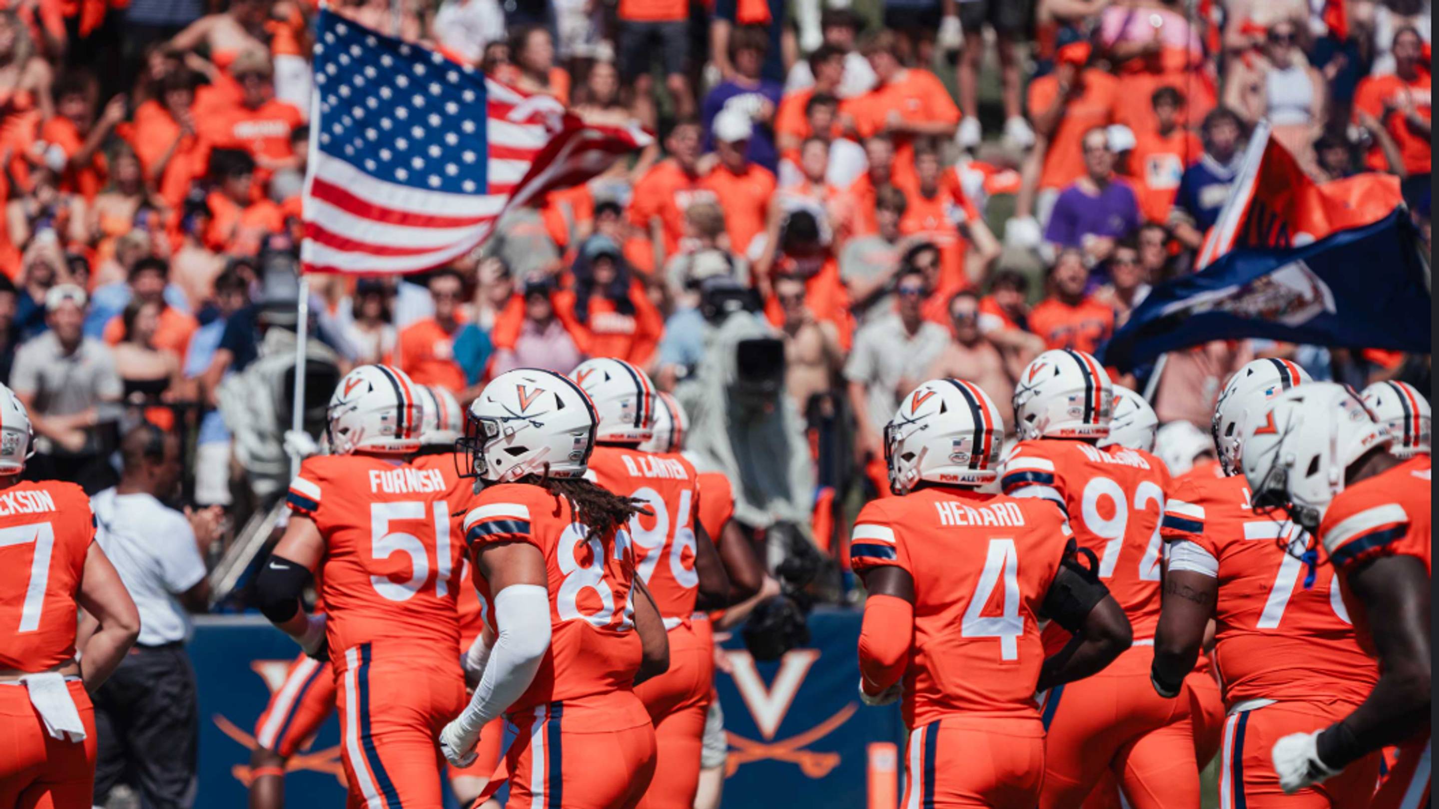 The Virginia Cavaliers charge onto the field, carrying the American flag.