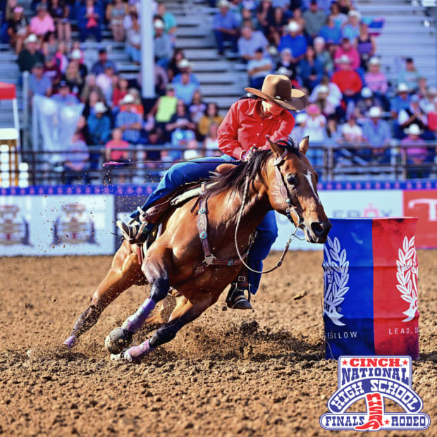 A high school aged barrel racer going around a barrel on a brown horse.