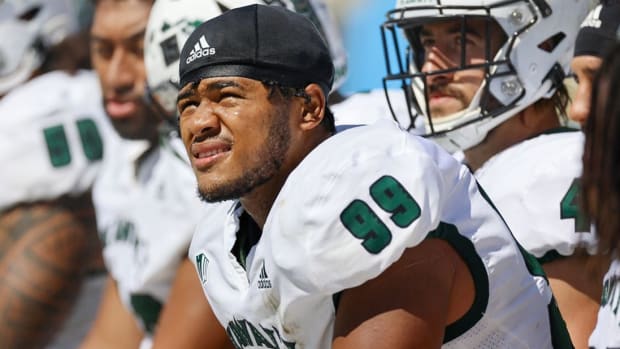 Football player Jonah Laulu looks on in a white jersey.