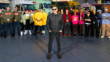 Nishaan, Fat Kid Food Co., Stop Drop N Roll, Rising Tiger, Good Fortune Company, Eat My Biscuits, Burger Walla, G’s Cheesesteaks and Cooking with Que team members in front of their trucks with host Tyler Florence, as seen on The Great Food Truck Race, Season 18.