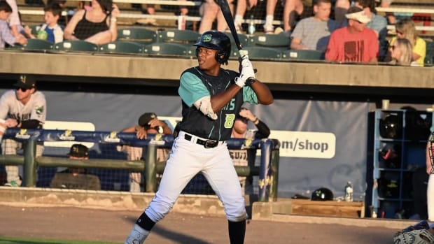 A baseball player wearing a navy and teal jersey, white pants, and a navy helmet while holding a baseball bat.