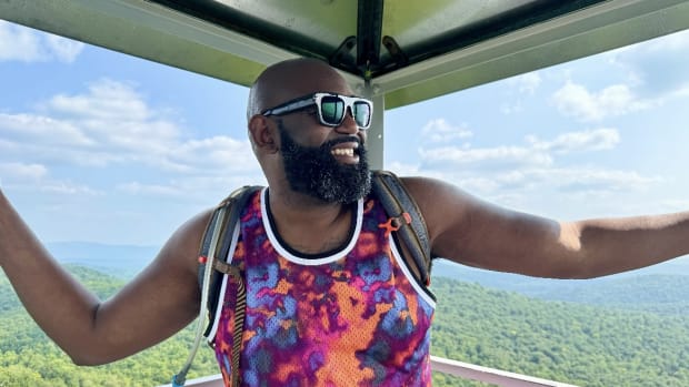 Clifton Harcum inside of Buck Mountain's summit firetower with the Adirondack mountains in the background.