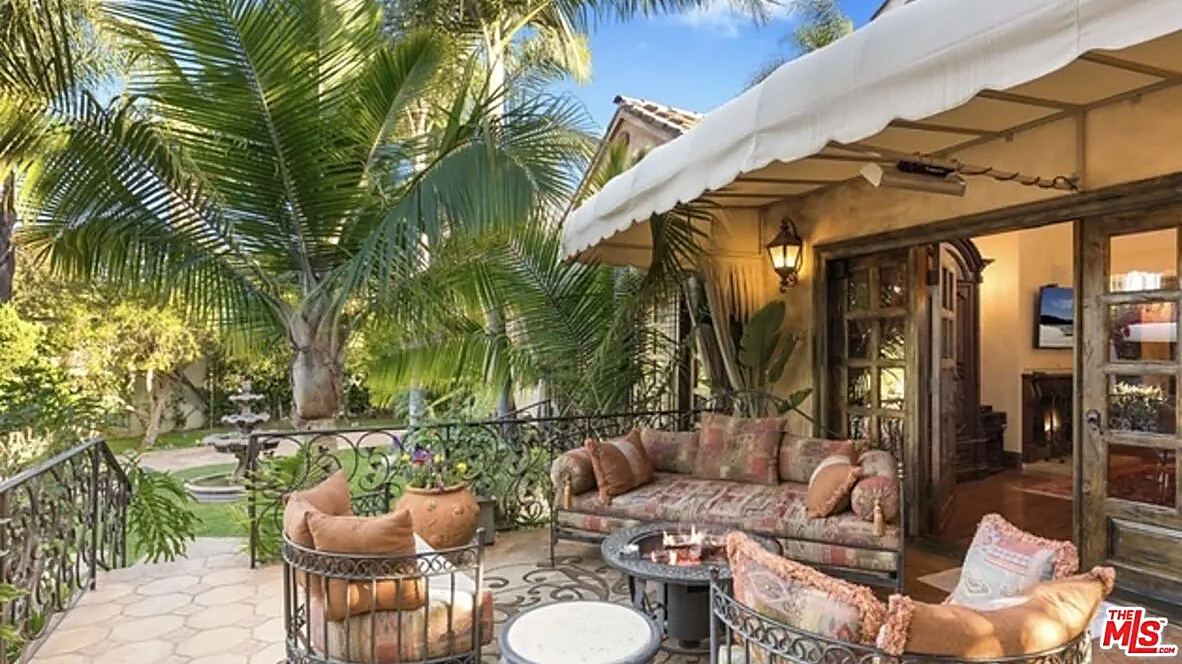A high end patio behind a nice home in California near USC with expensive furniture and a fire pit surrounded by palm trees.