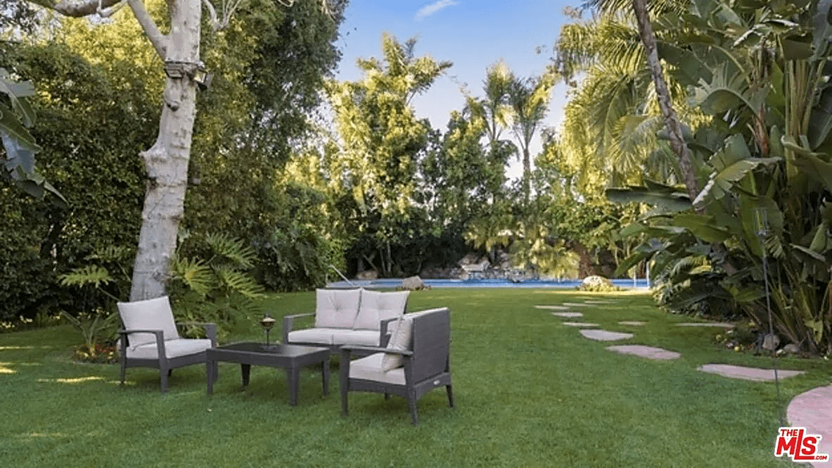 A lavish green back yard in Los Angeles with patio furniture and a pool surrounded by palm trees.