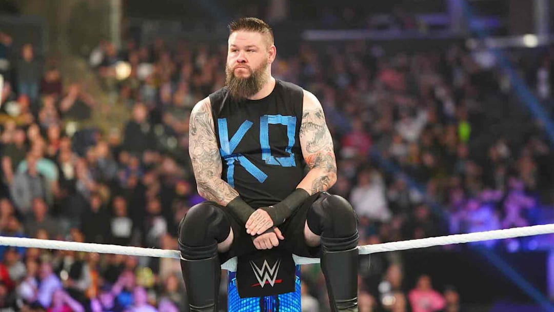 Kevin Owens sits on the middle rope while staring down his foe.
