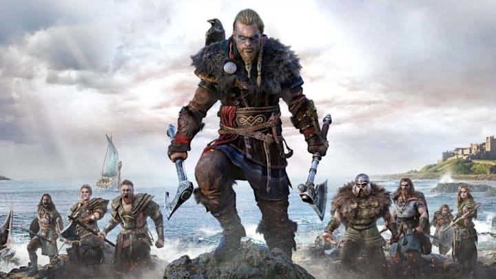 A Viking weilding two axes standing on a rock on a beach.
