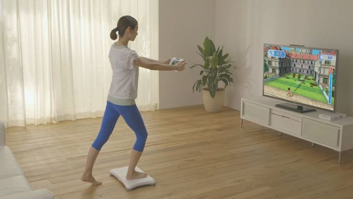 A woman standing with one foot on the Wii balance board holding a game pad out.