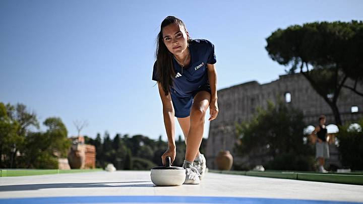 Serena Rota, instructora de curling, demuestra cómo lanzar la piedra mientras los participantes prueban este deporte de invierno en pistas sintéticas —sin hielo— instaladas en el parque Colle Oppio, con vistas al Coliseo, durante un caluroso día de verano. Serena Rota, instructora de curling, demuestra cómo lanzar la piedra mientras los participantes prueban este deporte de invierno en pistas sintéticas —sin hielo— instaladas en el parque Colle Oppio, con vistas al Coliseo, durante un caluroso día de verano.