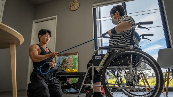 Hokuto Tatsumi (Izq) ayuda a una mujer adulta a entrenar en su casa. Hokuto Tatsumi (Izq) ayuda a una mujer adulta a entrenar en su casa.