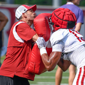 Arkansas Razorbacks wide receivers coach Antonio Jordan delivers a block to wide receivers coach Ronnie Fouch holding blocking shield in fall camp practices on the outdoor fields in Fayetteville, Ark.