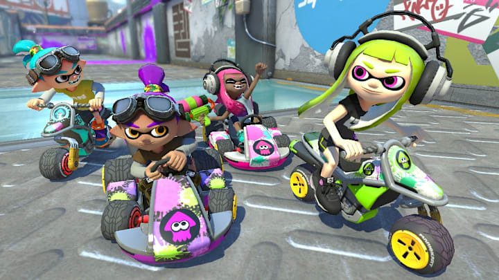 Four Inklings from Splatoon riding on vehicles in Mario Kart 8 Deluxe. 
