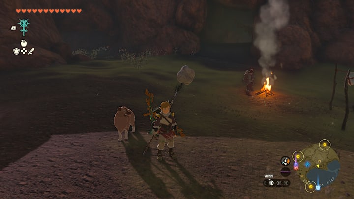 Link standing next to a dog near a campfire and a cave entrance.