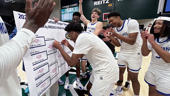 Mount Carmel basketball team celebrates as Tristen Wilson places the team’s name on the  championship bracket line. The Cougars defeated Mount Saint Joseph in Monday’s other semifinal for a chance to repeat as Baltimore Catholic League champions.