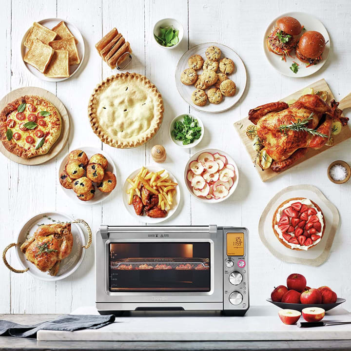Breville BOV900BSS Smart Oven Air Fryer Pro with various food dishes floating above it.