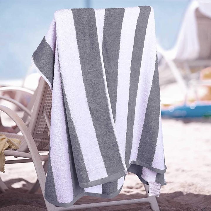 A gray and white striped Utopia beach towel draped over a chair on the beach.