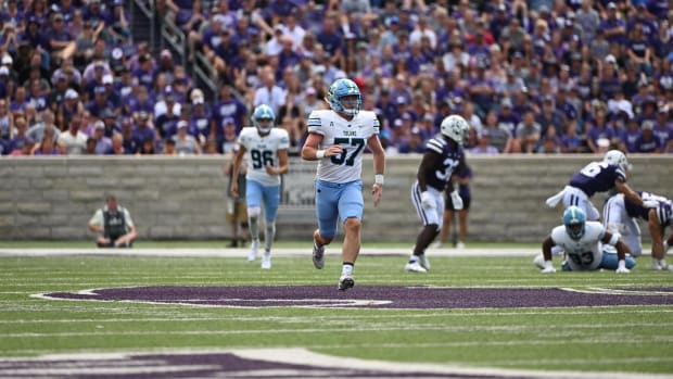 A football player runs on the field wearing a white jersey with green number and a blue helmet with blue pants.