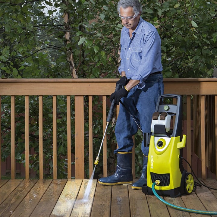 A Sun Joe SPX3000 electric pressure washer being used on a deck by a man.