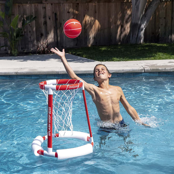Kid in a pool dunking a basketball into a Splash Hoop 360
