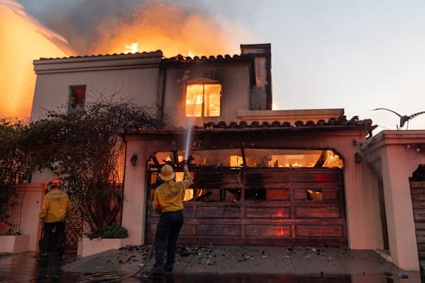 Firefighters attempt to extinguish a fire in a home along the Pacific Coast Highway in the Pacific Palisades neighborhood on 