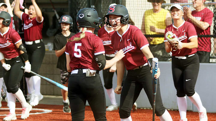 Sherwood senior Carmyn Knight (5) is greeted by junior Maisy Schindler after scoring the Bowmen’s second run in their 3-1 state playoff quarterfinal win over West Linn.