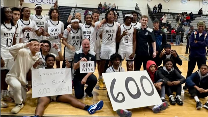 Surrounded by his players, Meade's Mike Glick holds up sign celebrating his 600th career win as a high school basketball coach.