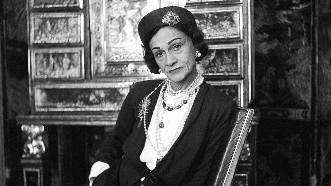 Designer Gabrielle "Coco" Chanel, wearing her signature pearls and jeweled pillbox hat, photographed by Cecil Beaton in 1953.