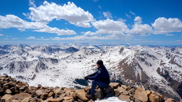 A person overlooking the peak of Mount Elbert with snow surrounding them on the rocks.