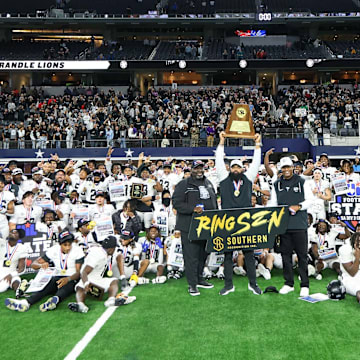 Richmond Randle head coach Brian Randle hoist the trophy while surrounded by coaches and players following their victory over South Oak Cliff in Texas 5A Division 2 title game at AT&T Stadium.