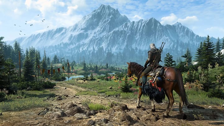 Geralt riding on Roach down a dirt path  in a field, with a forest and a  mountain in the distance.
