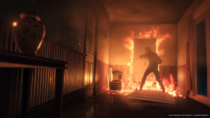 A man shields his face near a door surrounded by fire in The Evil Within 2