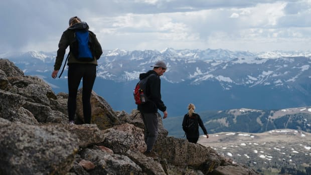 Three people are descending a mountain on rough terrain.