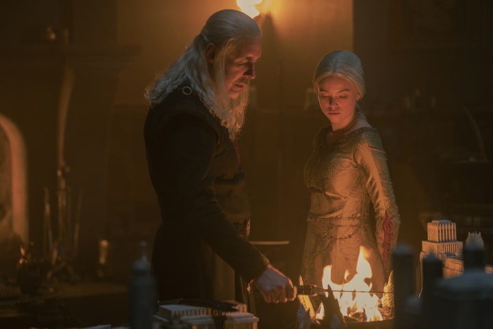 House of the Dragon season 1: Viserys holds Aegon the Conqueror's dagger over a brazier while young Rhaenyra watches.