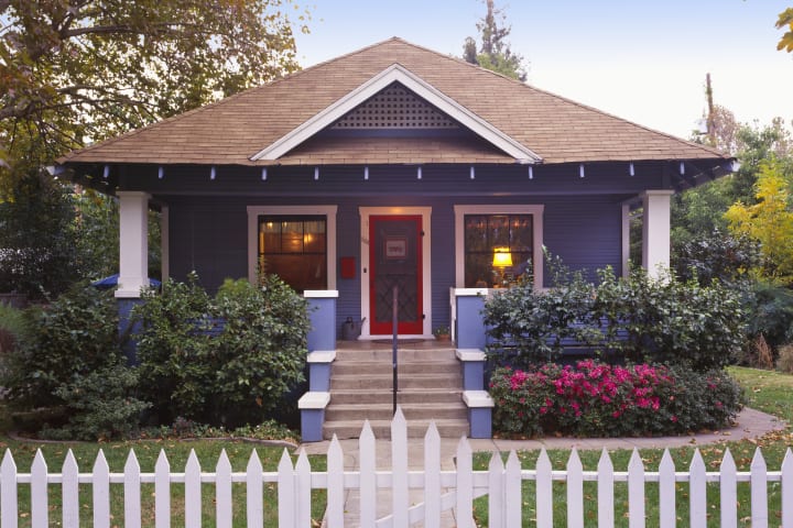 A blue Craftsman house with a white picket fence outside