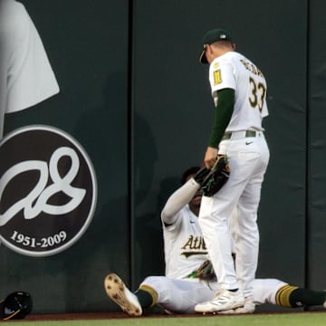 Jun 6, 2025; West Sacramento, California, USA; Athletics left fielder JJ Bleday (33) helps up center fielder Denzel Clarke (1) after he collided with the wall tracking down a deep fly ball by Baltimore Orioles shortstop Jorge Mateo during the fourth inning at Sutter Health Park. Mandatory Credit: D. Ross Cameron-Imagn Images